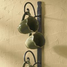 three tea cups are hanging from a metal rack on the wall next to a potted plant