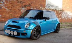 a small blue car parked in front of a brick building with graffiti on the walls