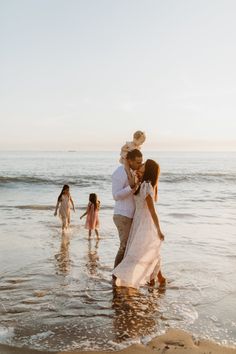 a man and woman hug while standing in the water at the beach with their children