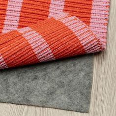 an orange and white checkered blanket laying on top of a wooden floor next to a gray rug