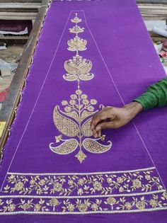 a woman is working on an intricately designed purple cloth with gold thread and sequins