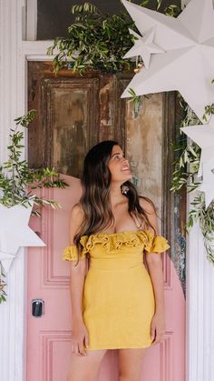 a woman standing in front of a pink door wearing a yellow dress with ruffles