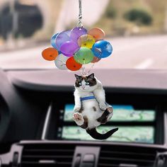 a cat hanging from a bunch of balloons in the air on a car dash board