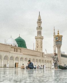 two men sitting on the ground in front of a building with green domes and minarets