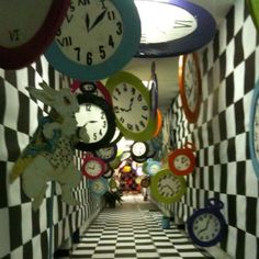 several clocks are hanging from the ceiling in an office hallway with black and white checkered walls