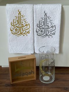 two white towels with arabic writing on them next to a box and glass filled with water