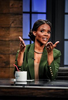 a woman sitting at a table with her hands in the air and pointing to something