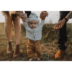 a baby is holding the hand of an adult's leg as they walk through grass