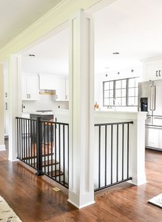 an open kitchen and living room with white walls, wood floors and black iron railings