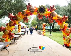 an archway decorated with balloons and stars in the middle of a sidewalk area at a park