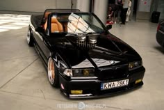 a black car parked in a garage next to another car with its hood up and the top down