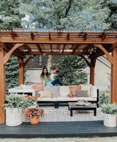 a woman sitting on top of a white couch under a wooden pergoline covered patio