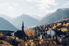 a small town surrounded by mountains and trees in the foreground, with a church steeple on top