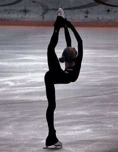 a woman skating on an ice rink with her arms in the air and one leg up