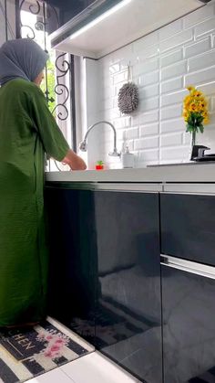 a woman in a hijab is washing dishes in the kitchen with flowers on the counter