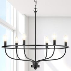 a black chandelier with five candles hanging from it's center and two windows in the background