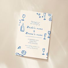 a white and blue wedding card with wine glasses on it next to a glass of champagne