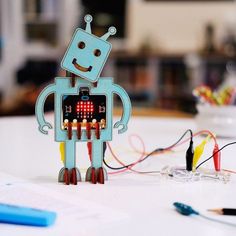 a robot made out of electronics sitting on top of a table next to some pens and pencils