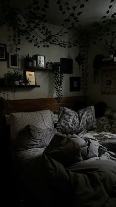 an unmade bed in a dark room with lots of plants on the wall above it