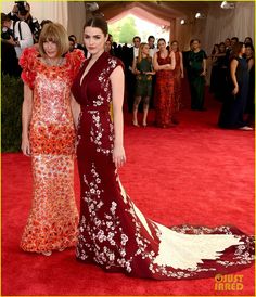 two women standing next to each other on a red carpet with people in the background