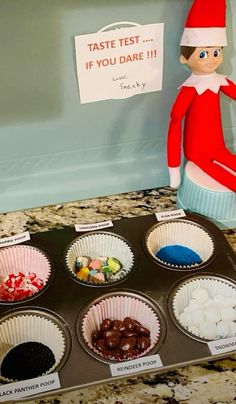 an elf is sitting on top of a muffin tin filled with candies and marshmallows