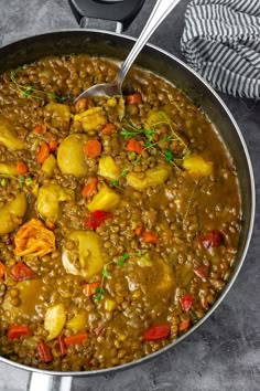 a pot filled with lentils and potatoes on top of a table next to a spoon