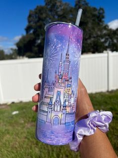 a hand holding a purple tumbler with a castle on it and fireworks in the sky