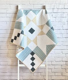 two quilts on a chair against a brick wall, one is blue and the other is white