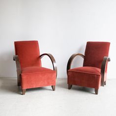 two red chairs sitting next to each other on a white floor in front of a wall