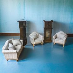 three chairs and two end tables in front of a blue wall with a clock on it