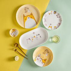 three plates with cats on them sitting next to some spoons and forks in front of a yellow and green background