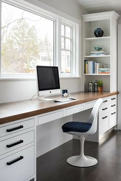 a desk with a computer on top of it in front of a window and bookshelf