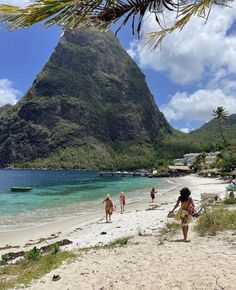 people are walking on the beach in front of some mountains and clear blue ocean water