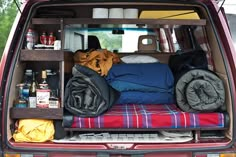 the back end of a red van filled with luggage and camping gear, including blankets