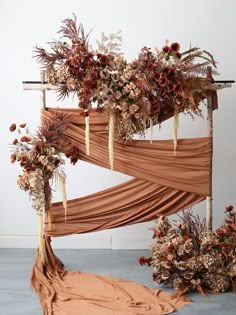 an arrangement of dried flowers and foliage on a wooden structure with drapes draped over it