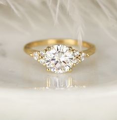 a close up view of a diamond ring on a white surface with feathers in the background