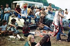 a group of people sitting on top of a grass covered field next to parked cars