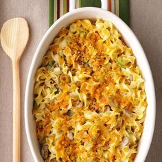 a white bowl filled with macaroni and cheese on top of a table next to a wooden spoon