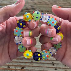 two hands holding different colored beads in each other's palms, one with multicolored dots on it