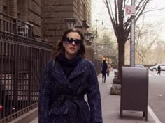 a woman is walking down the sidewalk with her suitcase in hand while wearing sunglasses and a coat