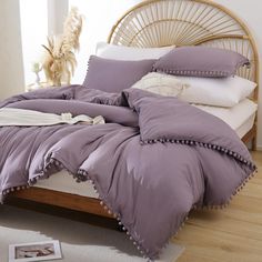 a bed with purple comforter and pillows on top of it in front of a window