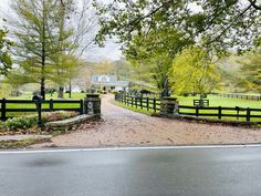 a gated driveway leading to a farm with a house in the background and trees on either side