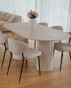 a table with chairs and a vase on it in front of a couch, near a window