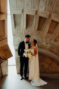 a bride and groom are standing in front of a stone arch with flowers on it