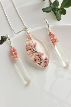 three pieces of jewelry sitting on top of a white plate next to a green plant