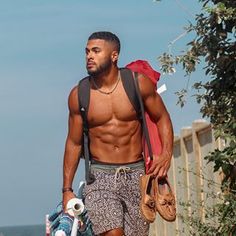 a shirtless man walking down the street with his skateboard and bag in hand