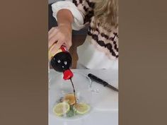 a woman pours orange juice into a glass with lemon slices on the side, while sitting at a table