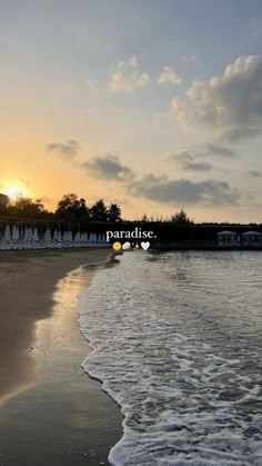 the sun is setting over an empty beach with water and umbrellas in the foreground