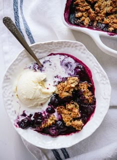 blueberry cobbler with ice cream in a white bowl on a towel next to another dish