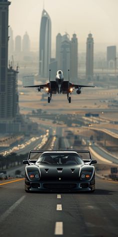 a black sports car driving down the road in front of a jet flying over a city